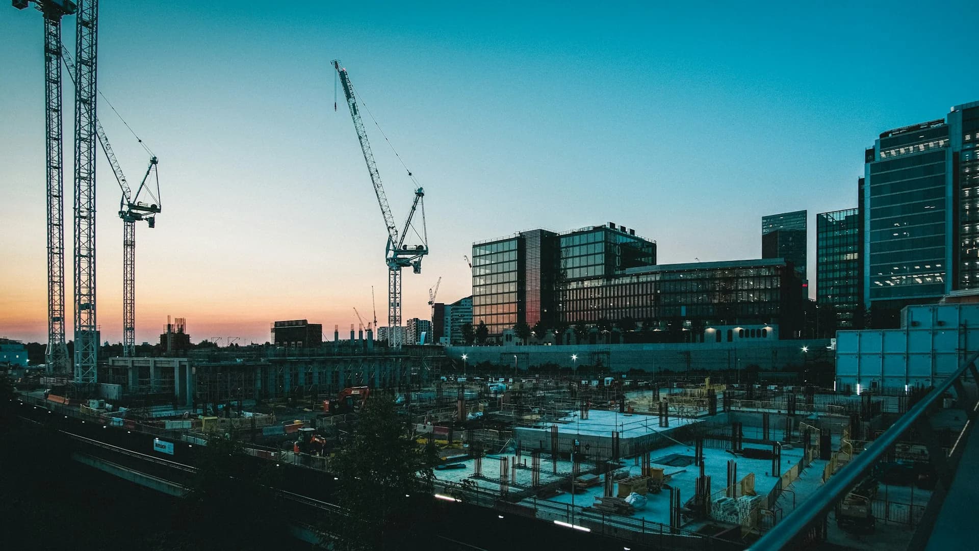 Gün batımında beton temeller üzerinde yükselen inşaat vinçleri